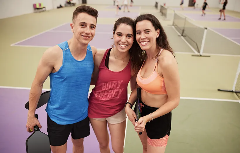 A group of three friends poses for the camera on the pickle ball court.